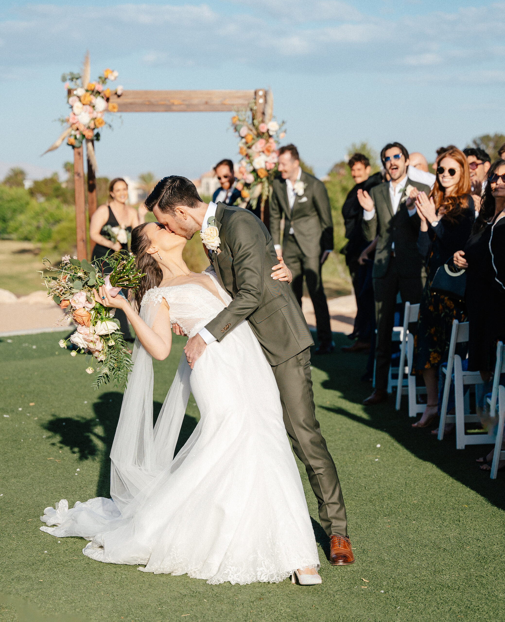 Groom dips bride for their first kiss under a floral arch at TPC Summerlin wedding in Las Vegas