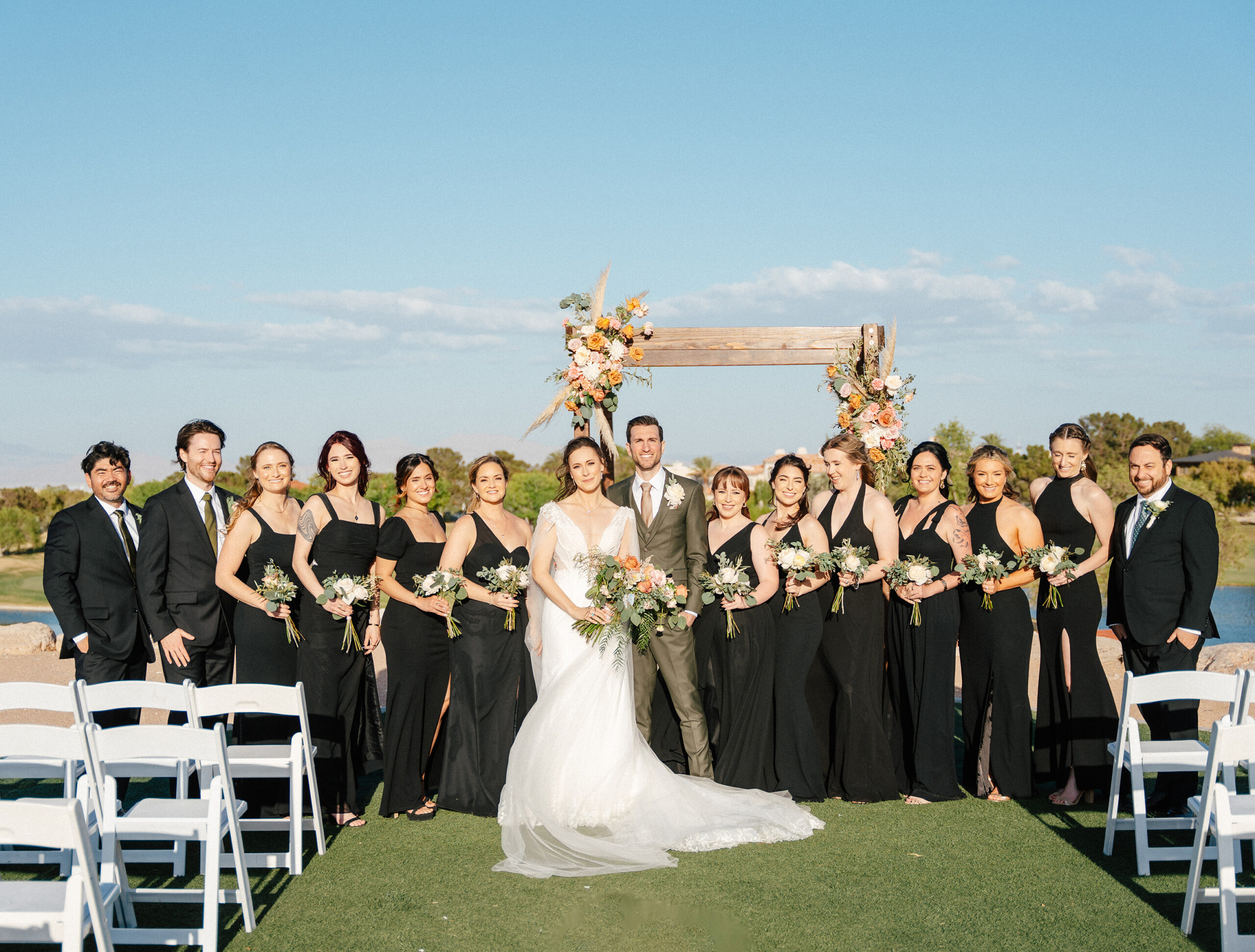 Bride, groom, bridesmaids, and groomsmen pose in front of a floral arch at TPC Summerlin wedding venue in Las Vegas