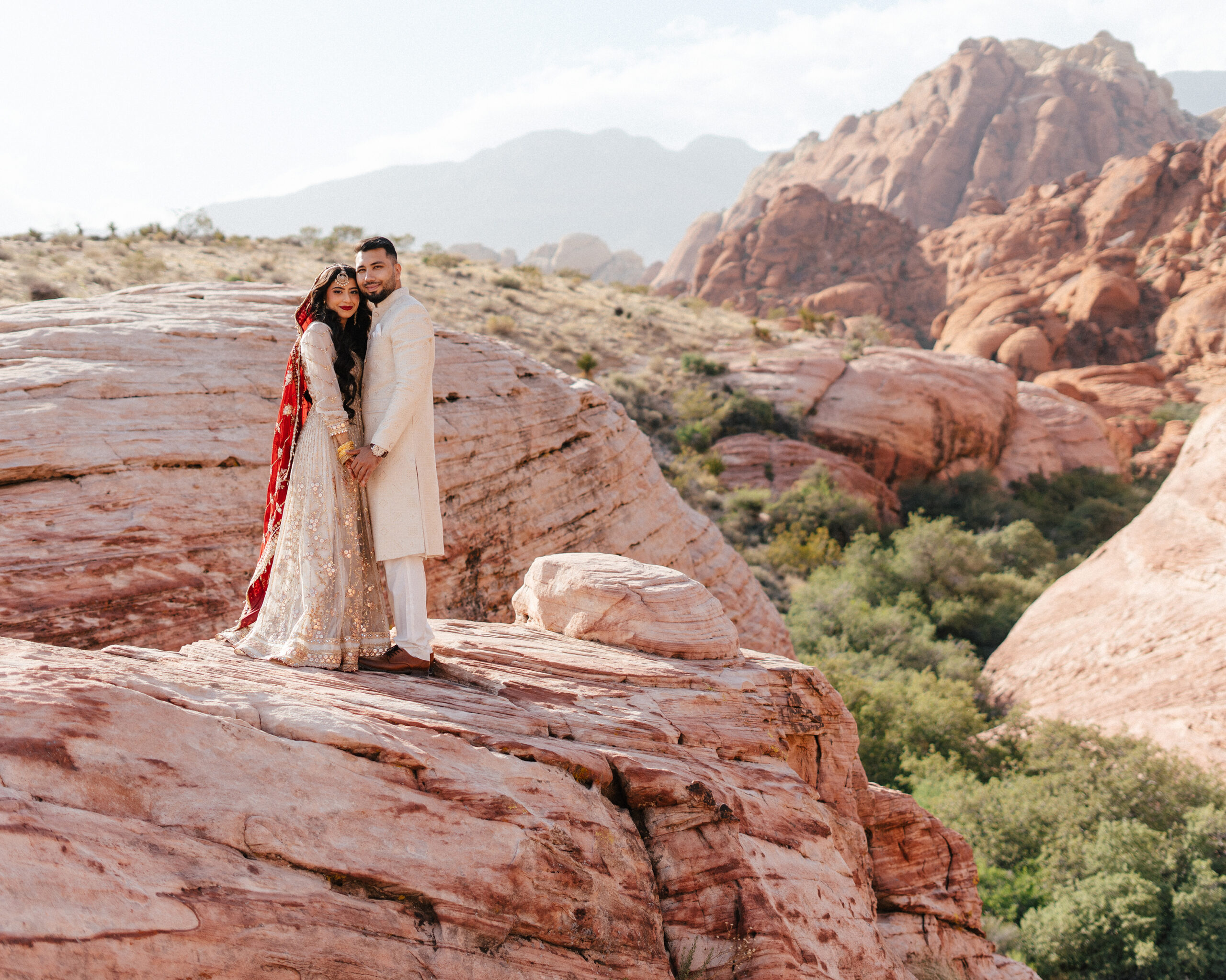 Bride and groom stand on a scenic overlook surrounded by red cliffs in their red rock canyon wedding photos