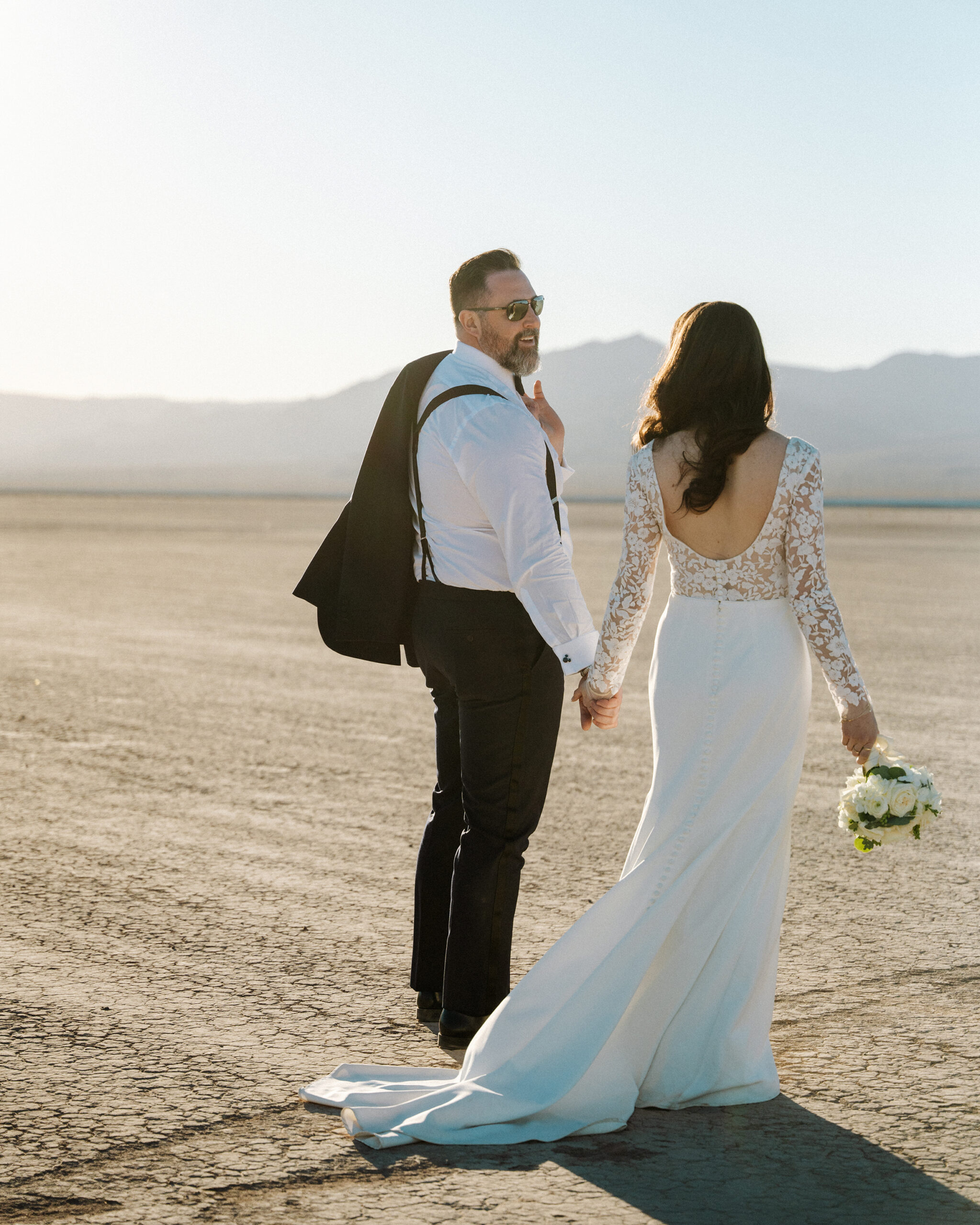 Groom in tuxedo walking across eldorado dry lake bed after Nelson Ghost Town wedding ceremony