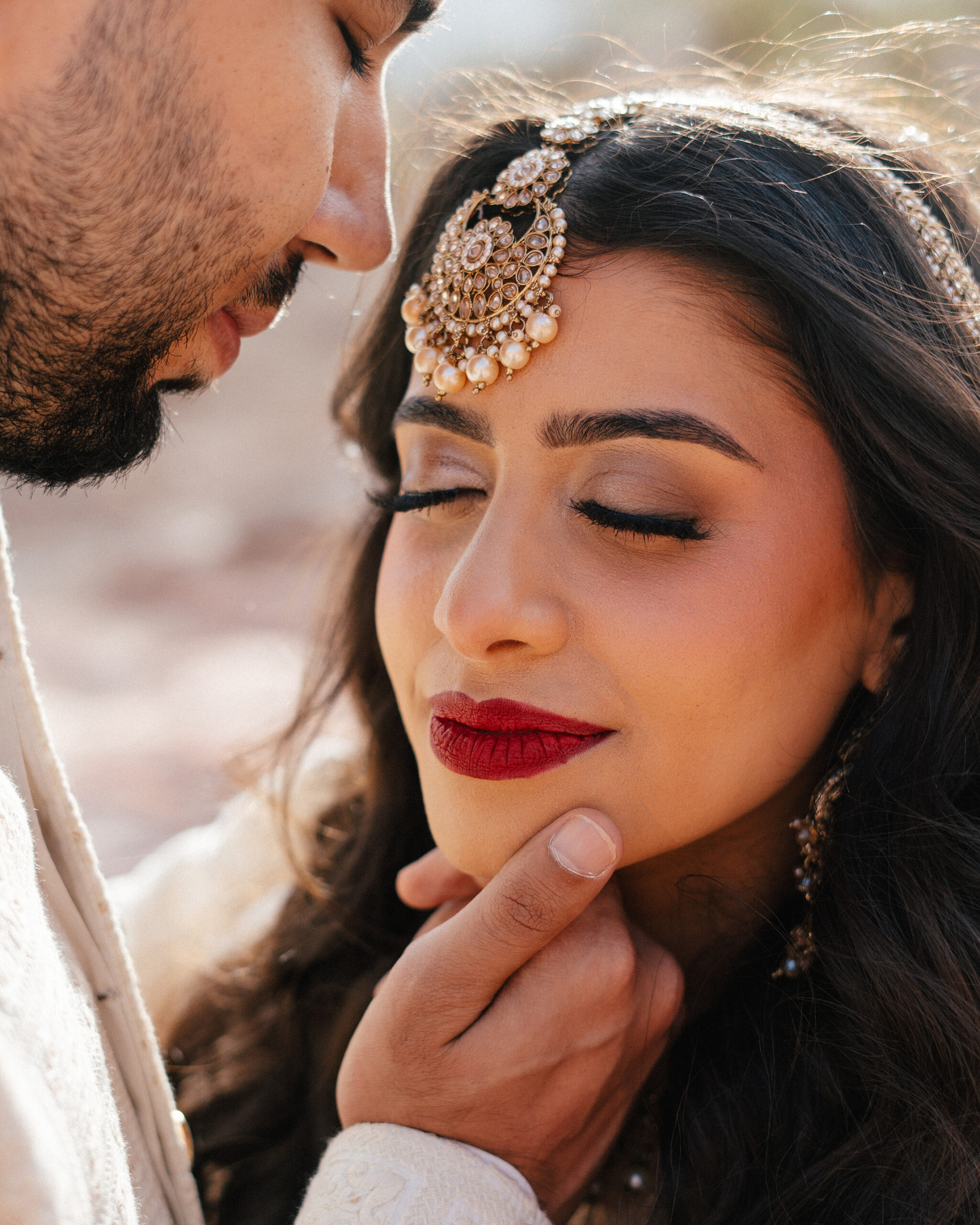 Groom gently holds the bride’s face as they lean in during red rock canyon wedding portraits