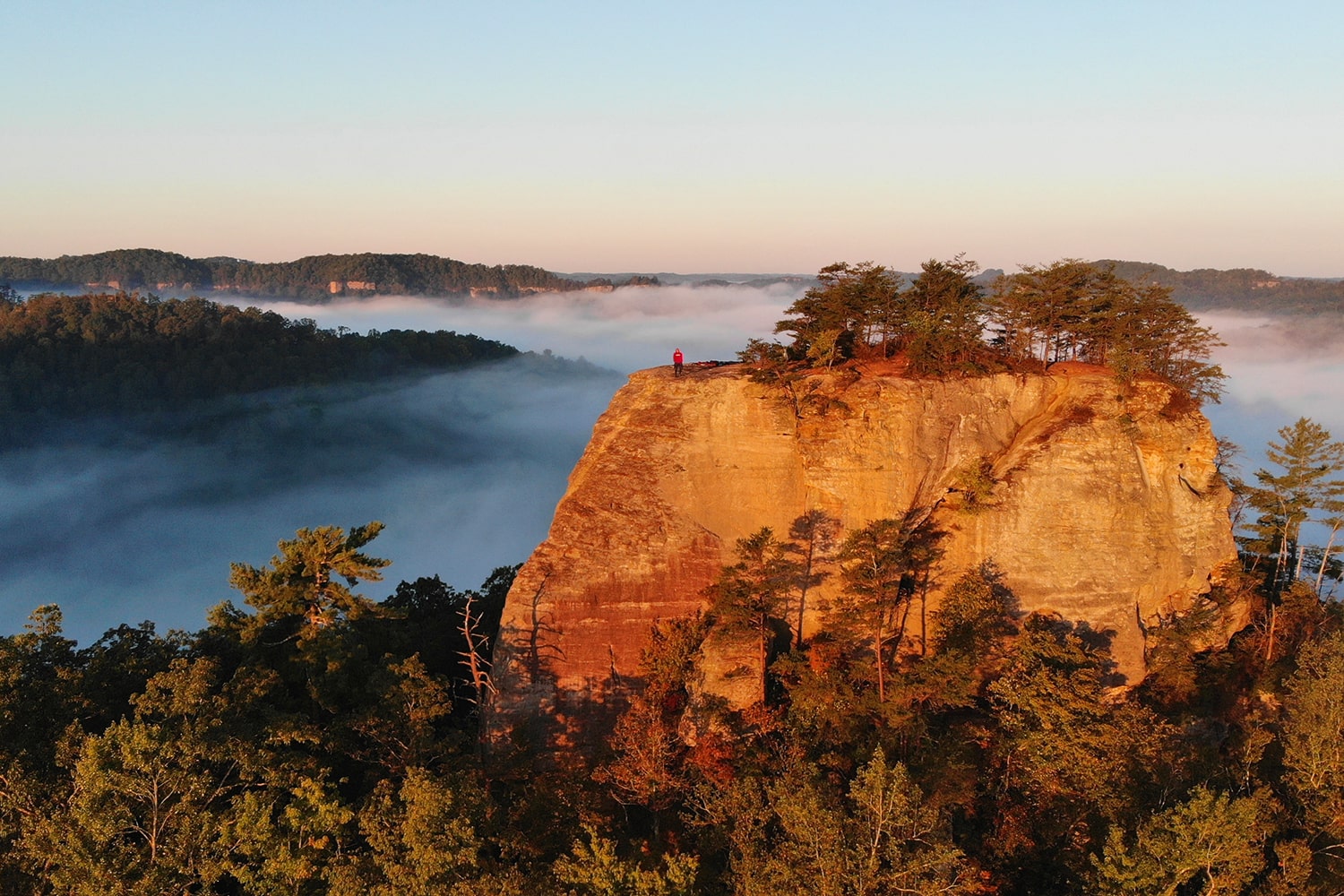 Dramatic sunrise view of a cliffside overlook in Red River Gorge, Kentucky, with mist-filled valleys and vibrant orange sandstone — an iconic wedding backdrop.