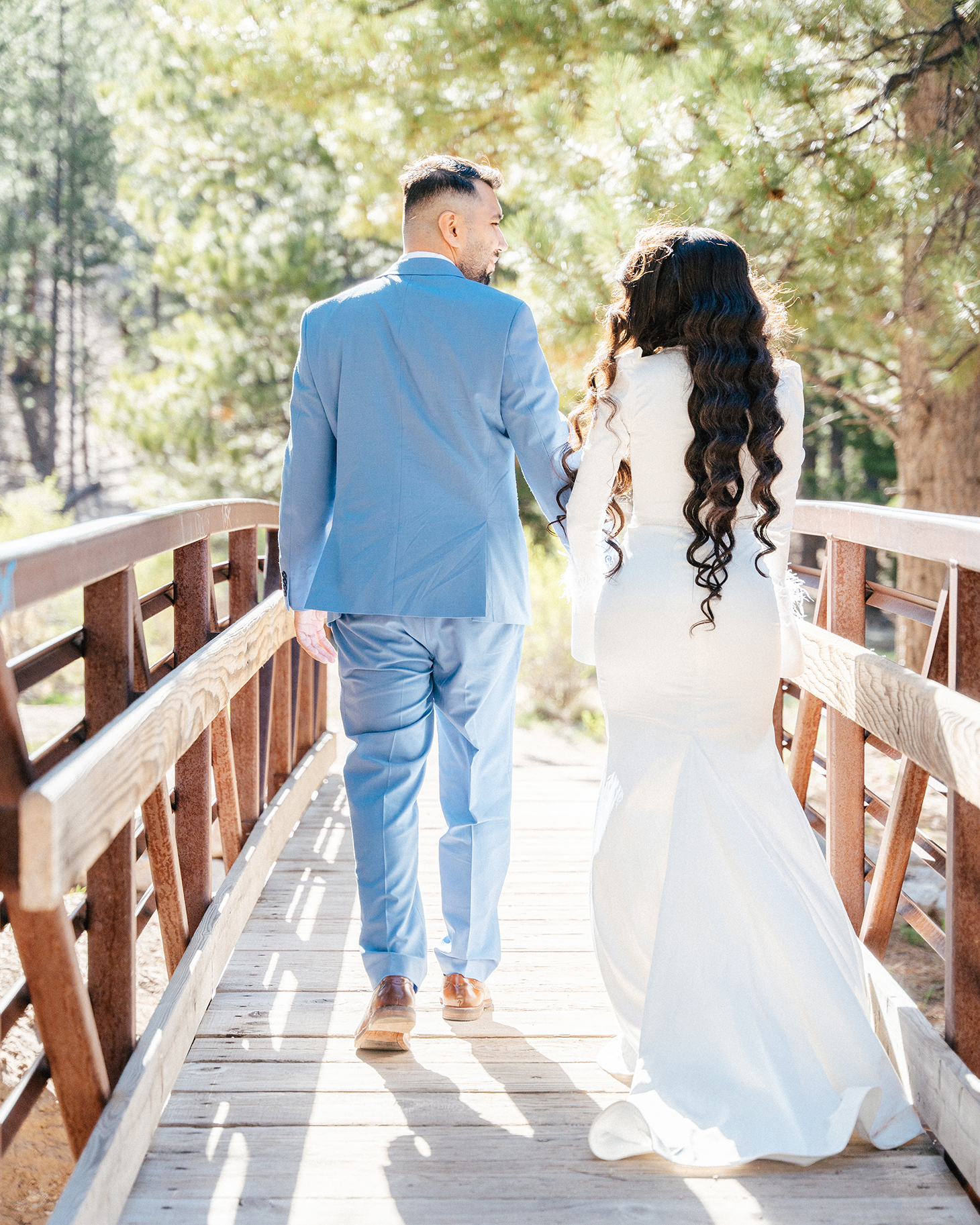 Bride and groom walking across a rustic wooden bridge surrounded by forest.