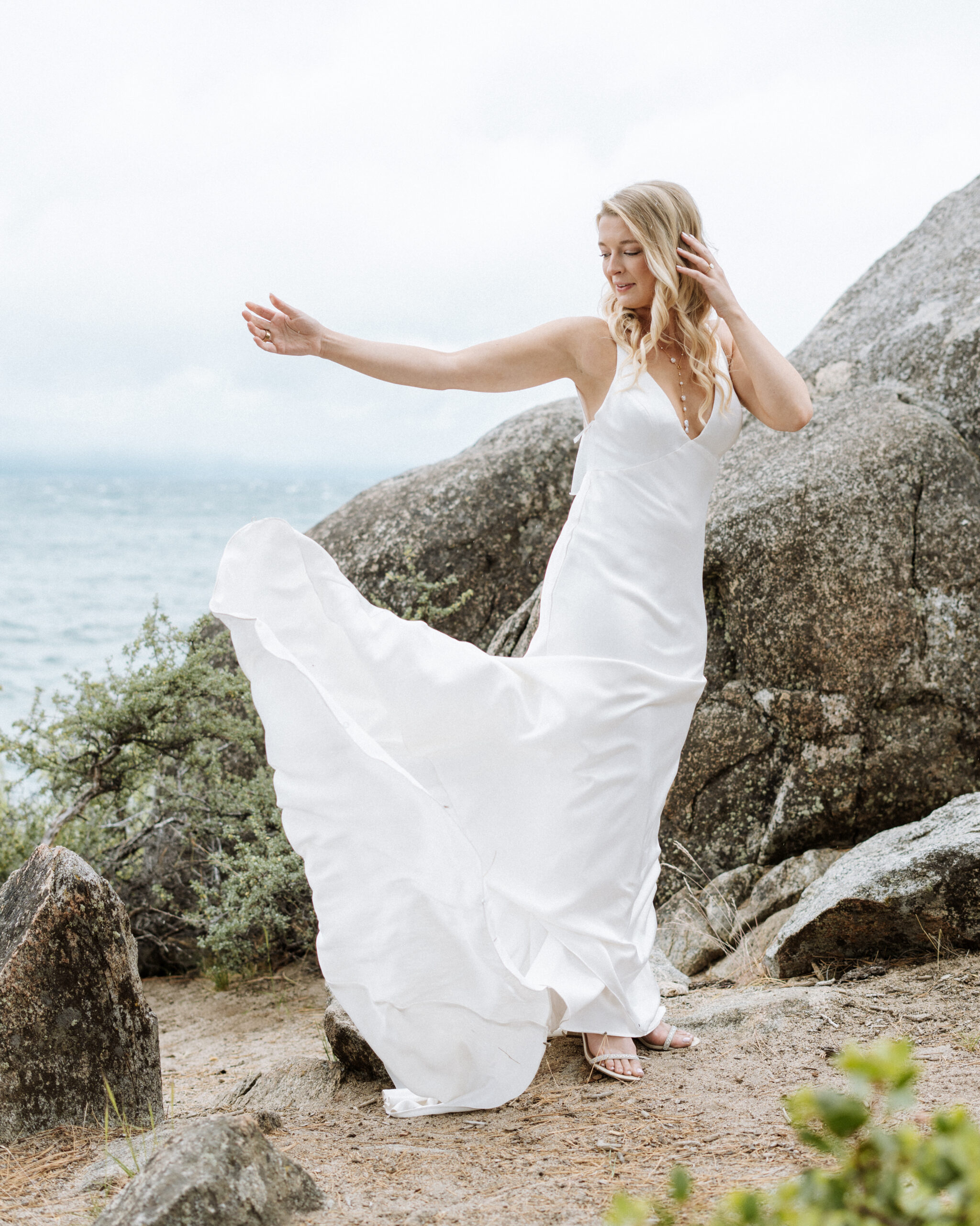  A bride dances gracefully on the rocky shore near The Arch at Lakeside Beach in South Lake Tahoe, capturing the beauty of her lakeside wedding day.