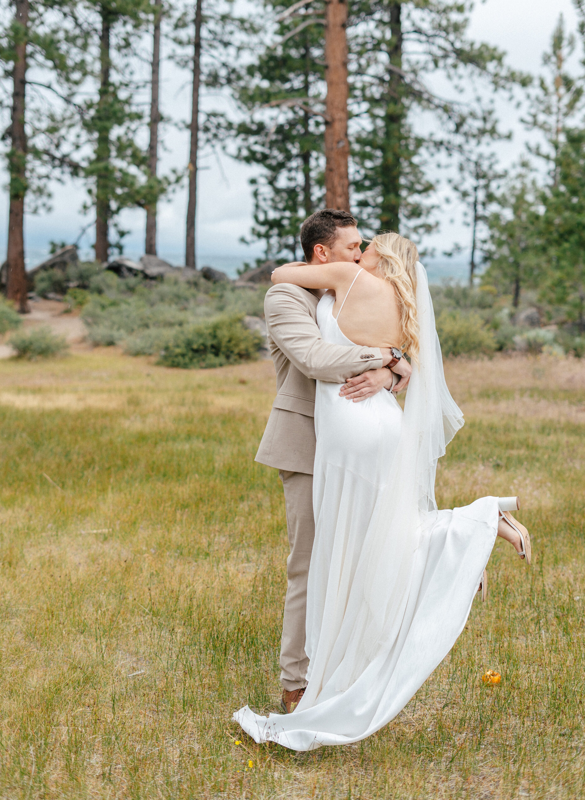 A joyful wedding moment in South Lake Tahoe as the bride leaps into the groom’s arms for a kiss, captured with forest views and lake air all around