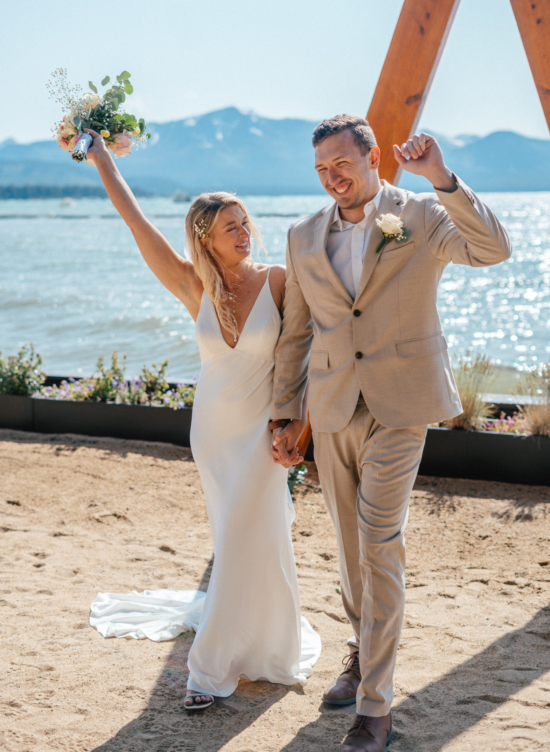 A beaming couple celebrates their South Lake Tahoe elopement at the stunning Lakeside Beach wedding venue, with mountain views and golden lakefront light