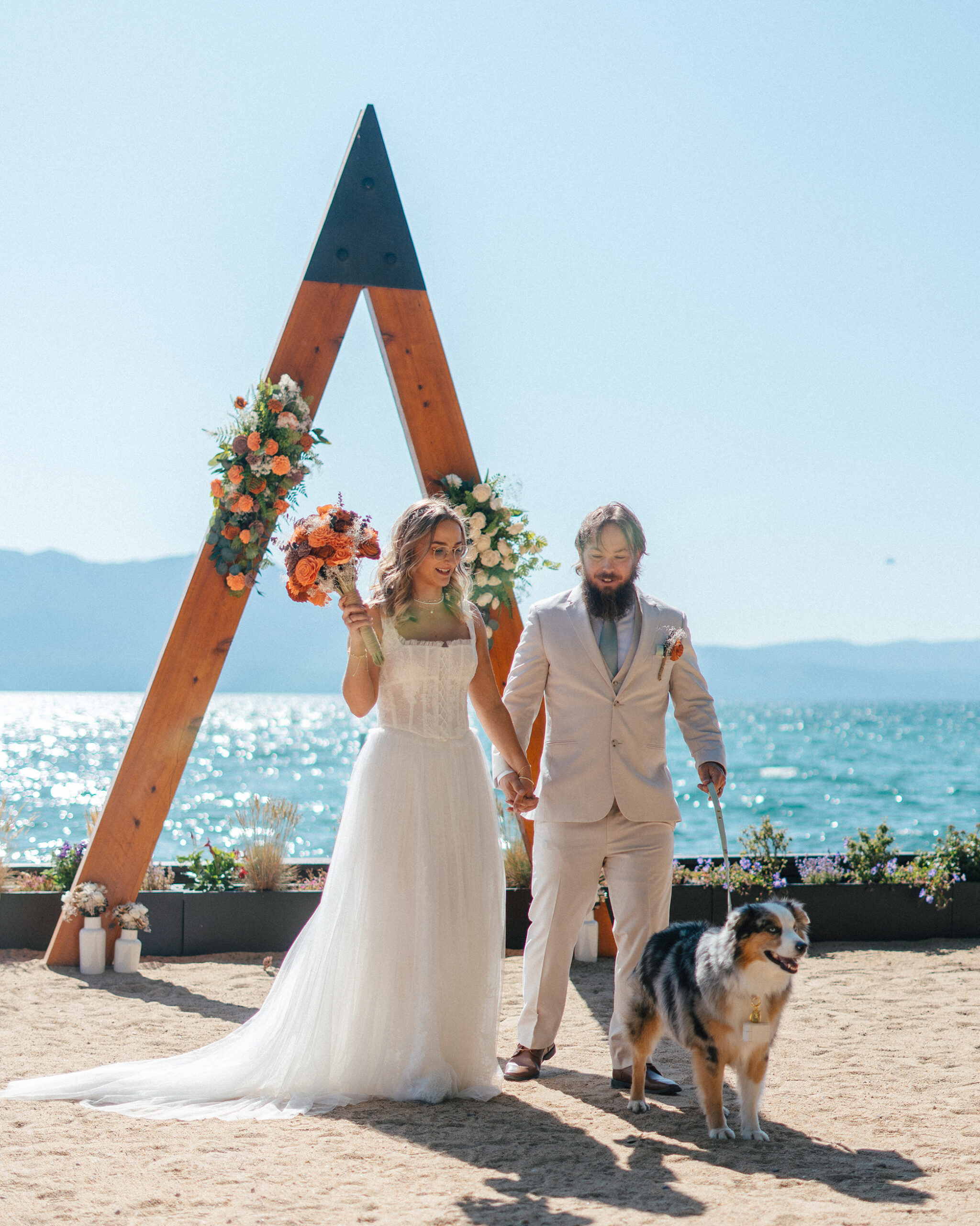 A joyful couple walks hand in hand with their dog after their Lake Tahoe beach ceremony.