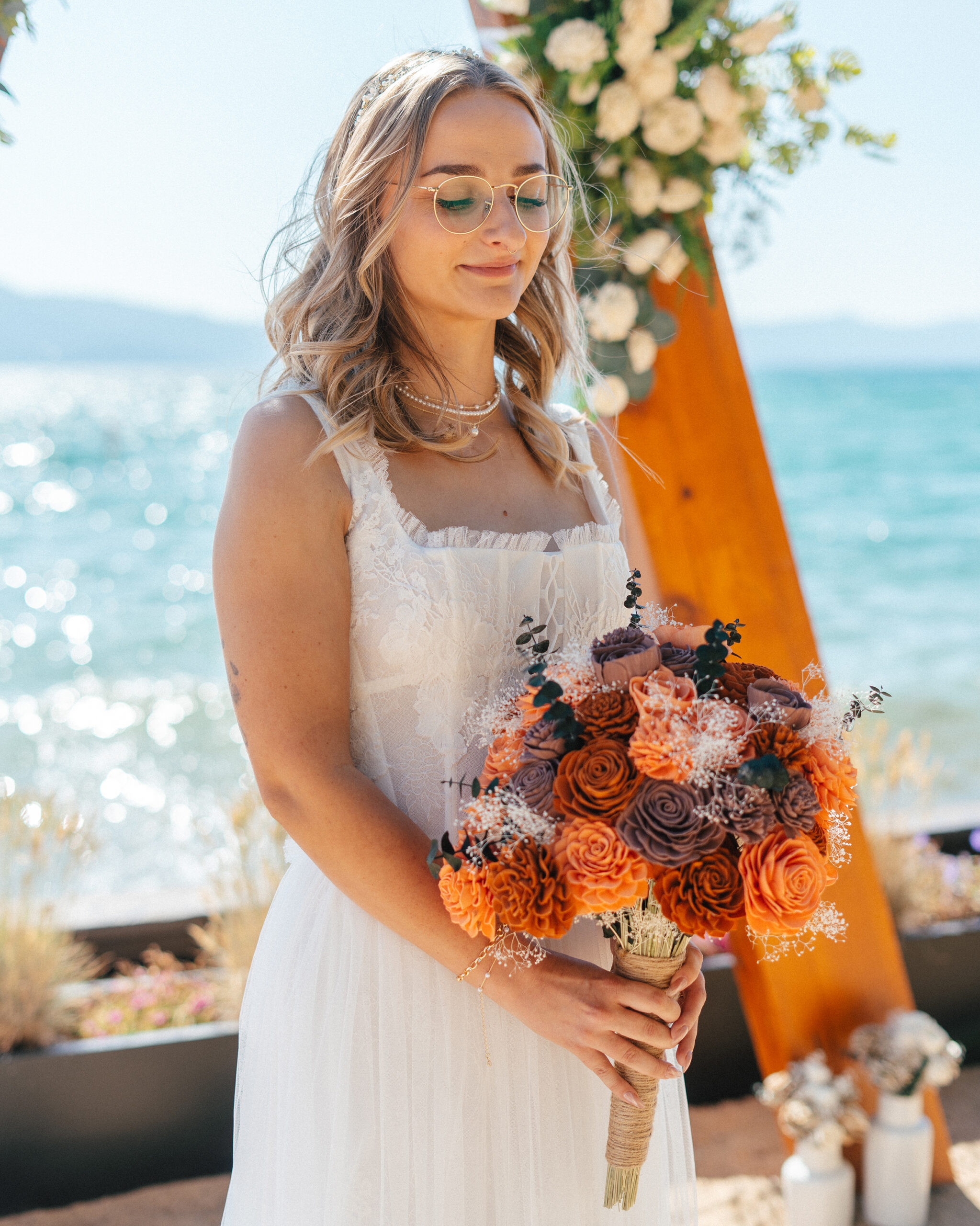The bride poses with a vibrant orange and lavender bouquet at Lakeside Beach.