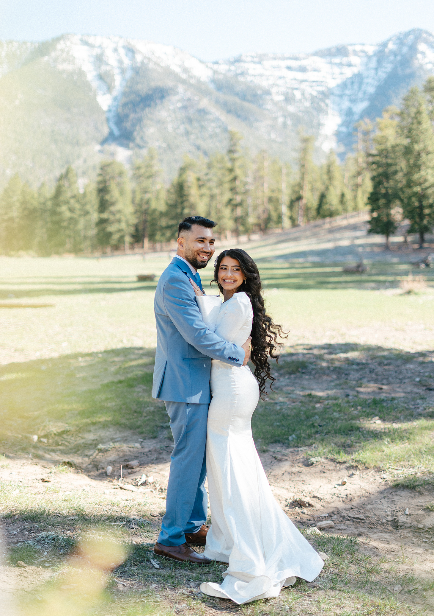 Bride and groom embrace under pine trees with snowy mountain backdrop at Lee Canyon.