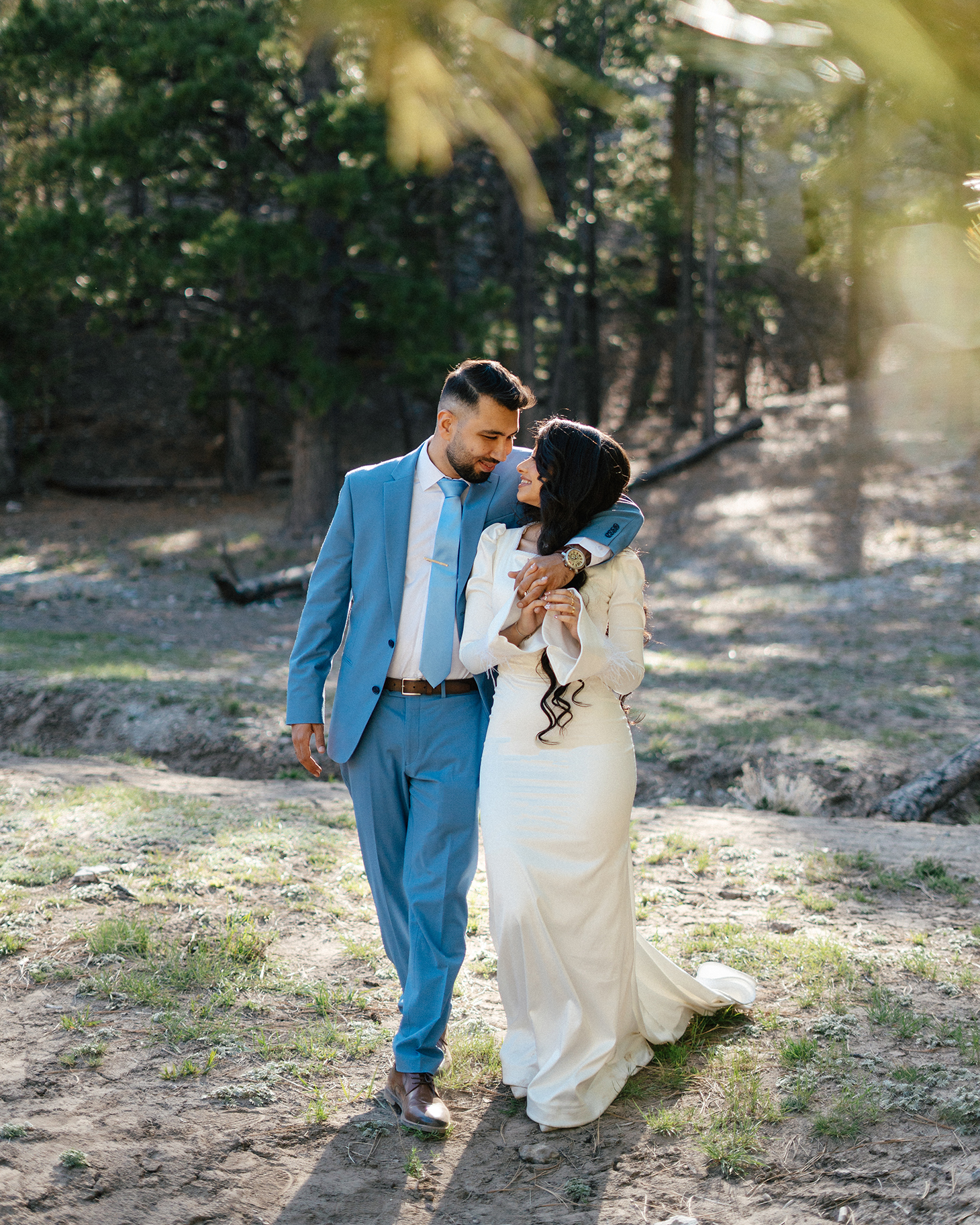 Groom gazes at bride as they walk hand-in-hand through pine forest at Lee Canyon.