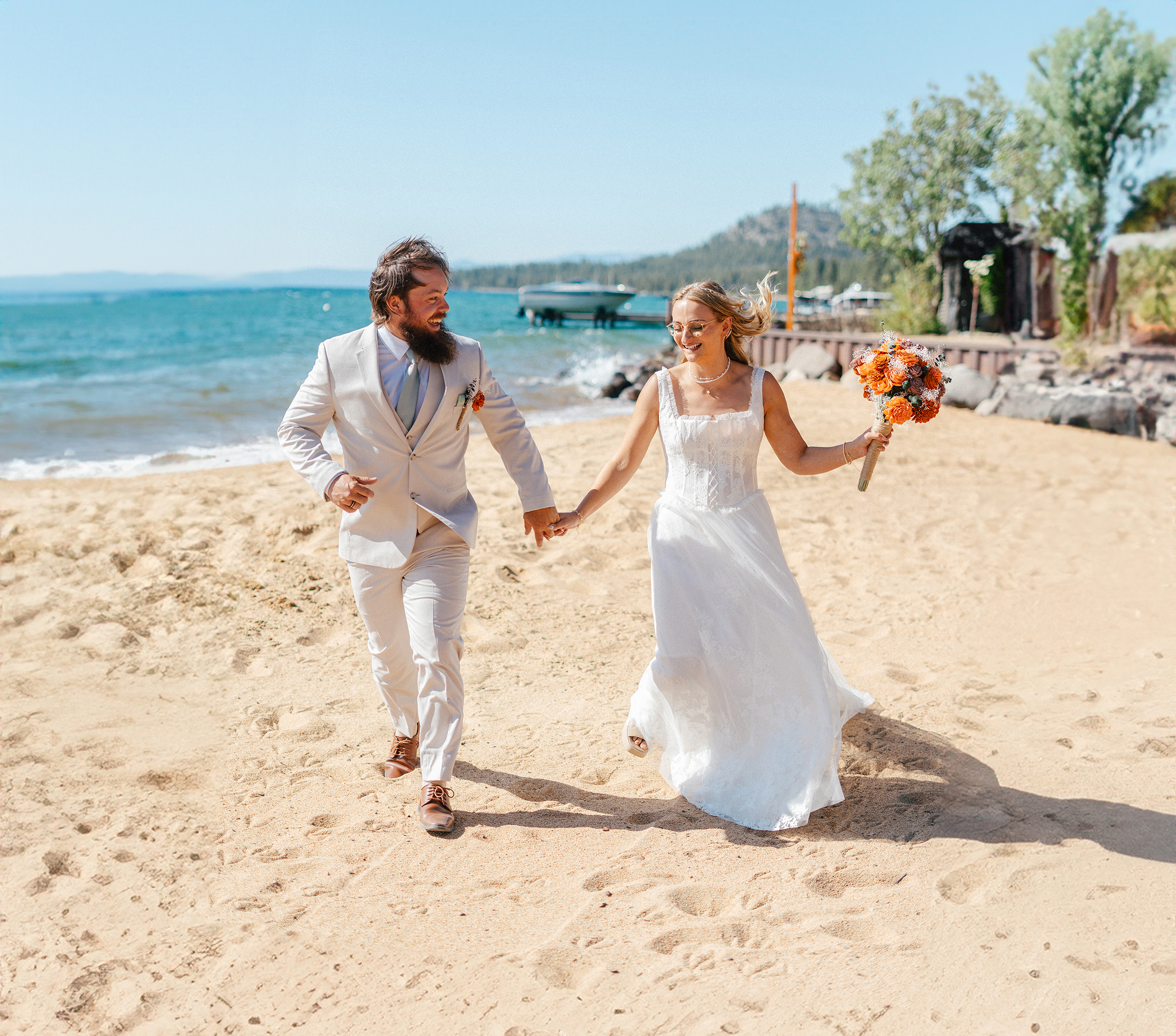 A bride and groom run hand-in-hand along the shore after their ceremony at Lakeside Beach in South Lake Tahoe.